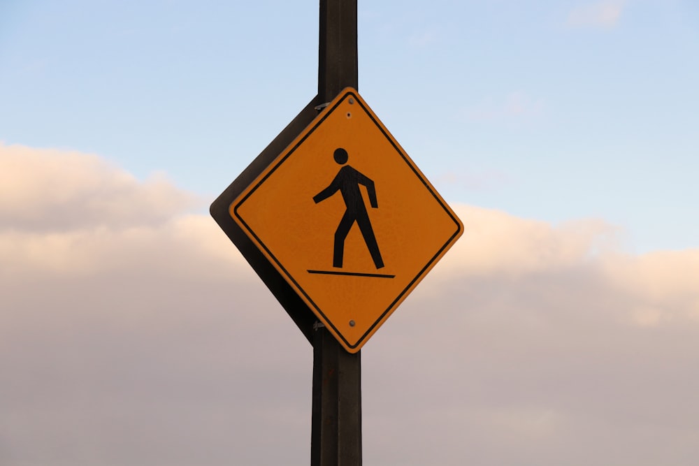 a yellow pedestrian crossing sign hanging from a wooden pole