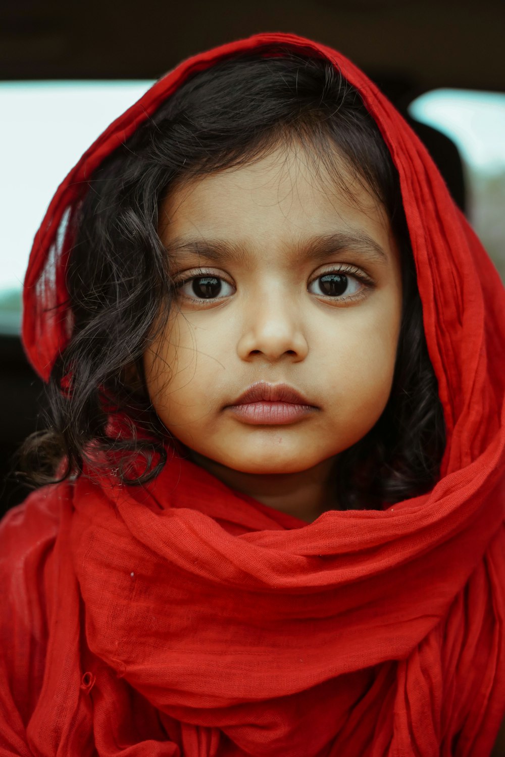 a little girl wearing a red scarf around her head