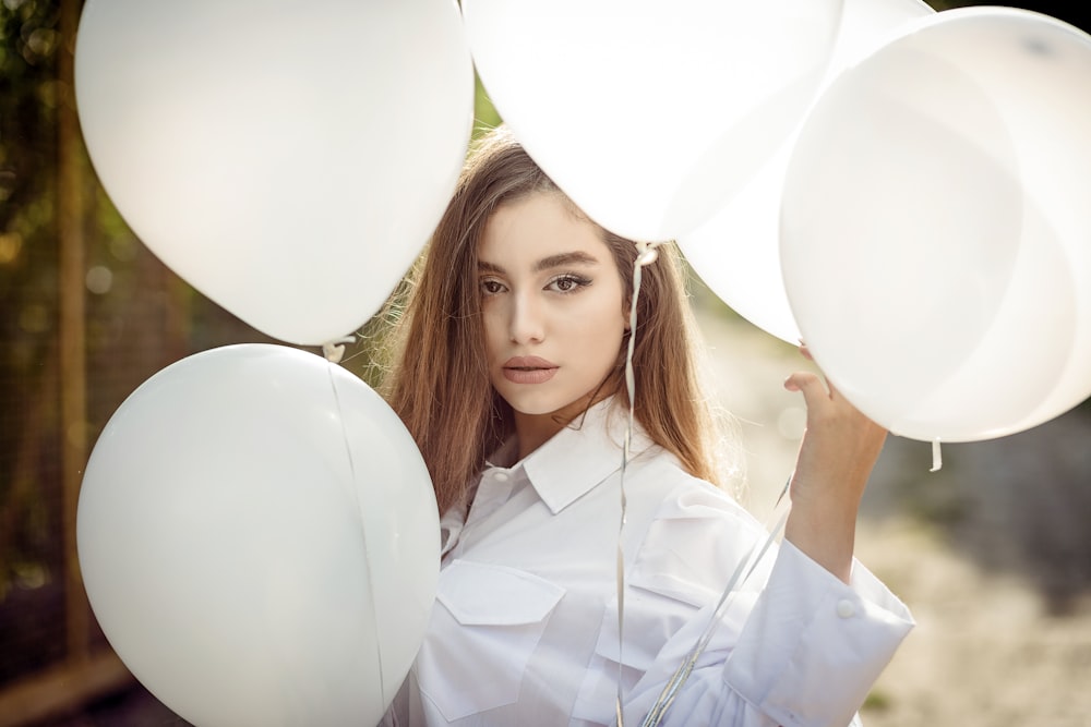 a woman holding white balloons in front of her face