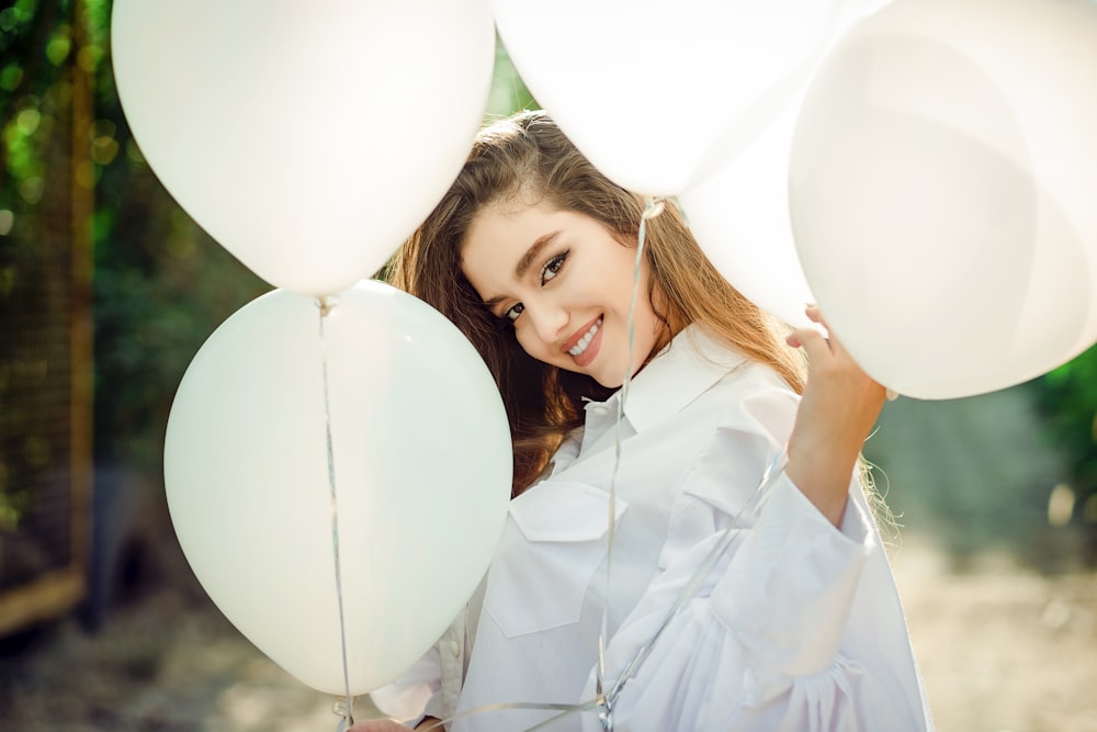 a woman holding a bunch of white balloons