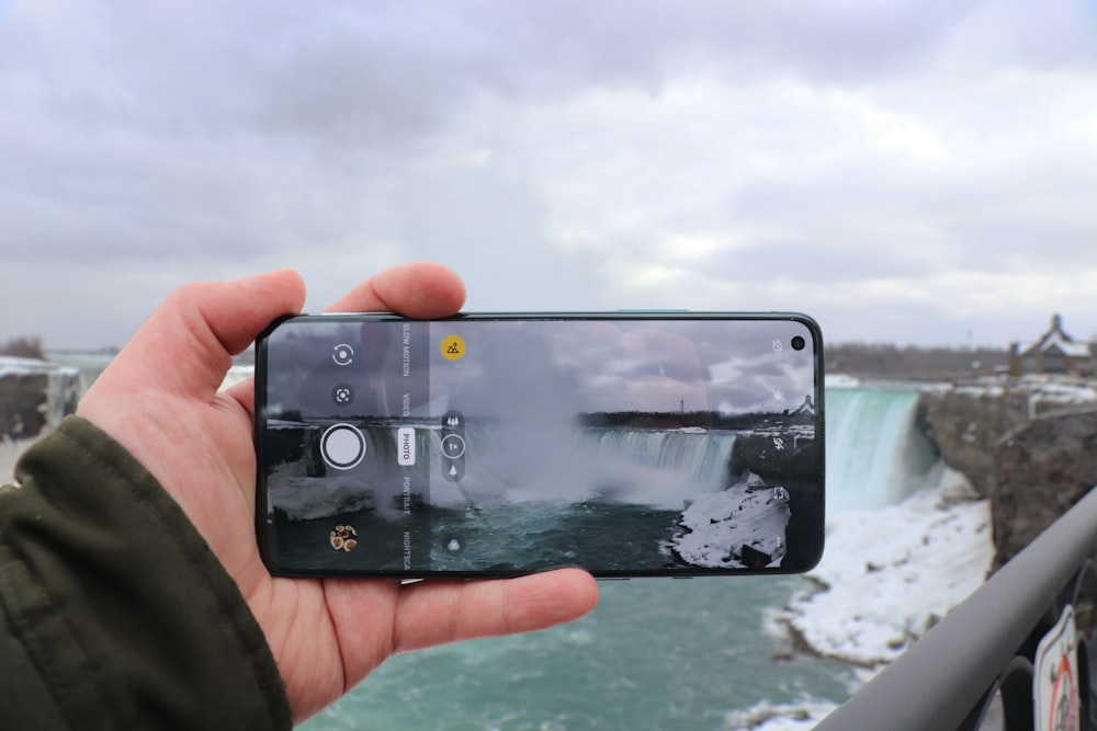 a person taking a picture of a waterfall with a cell phone