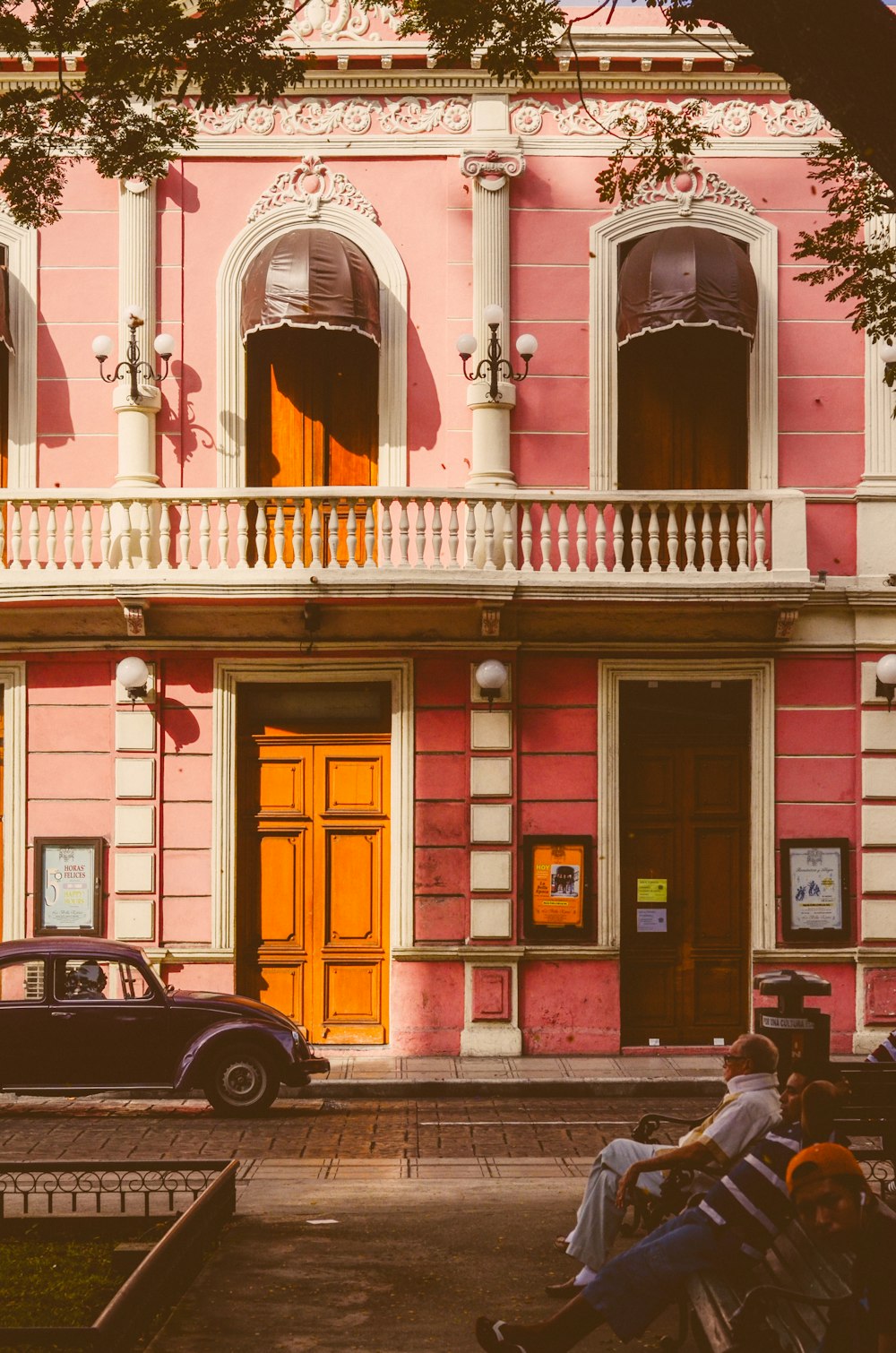 a group of people sitting on a bench in front of a pink building