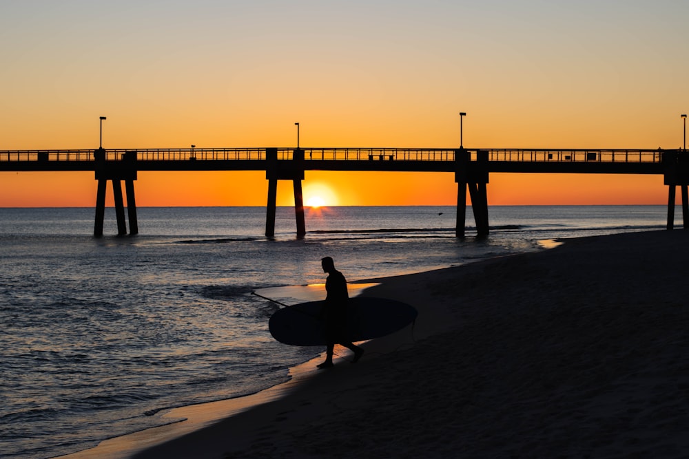 Eine Person, die bei Sonnenuntergang ein Surfbrett am Strand trägt