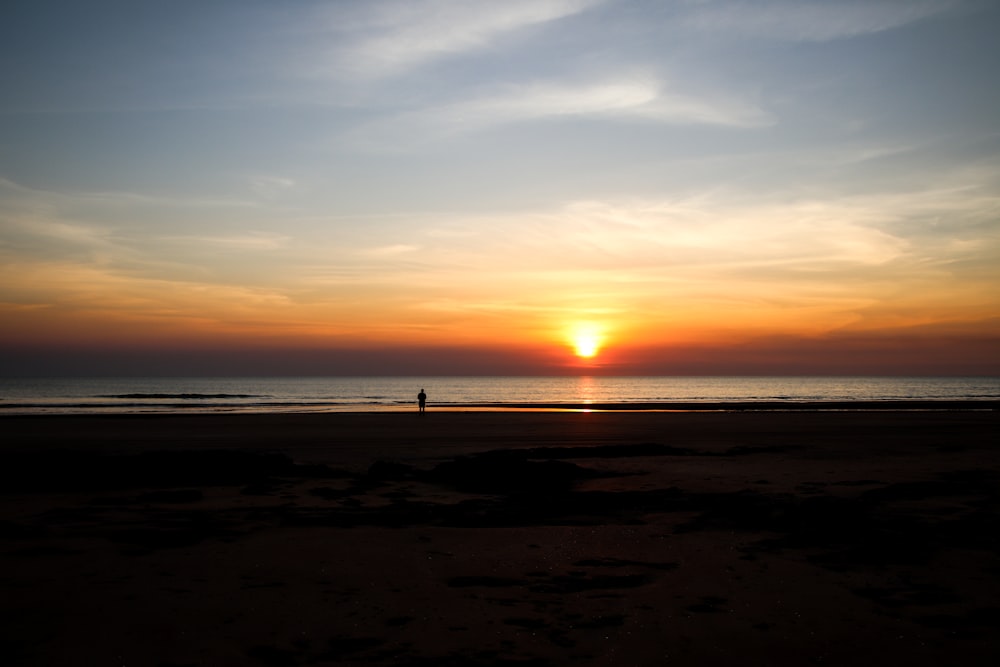 a person walking on a beach at sunset