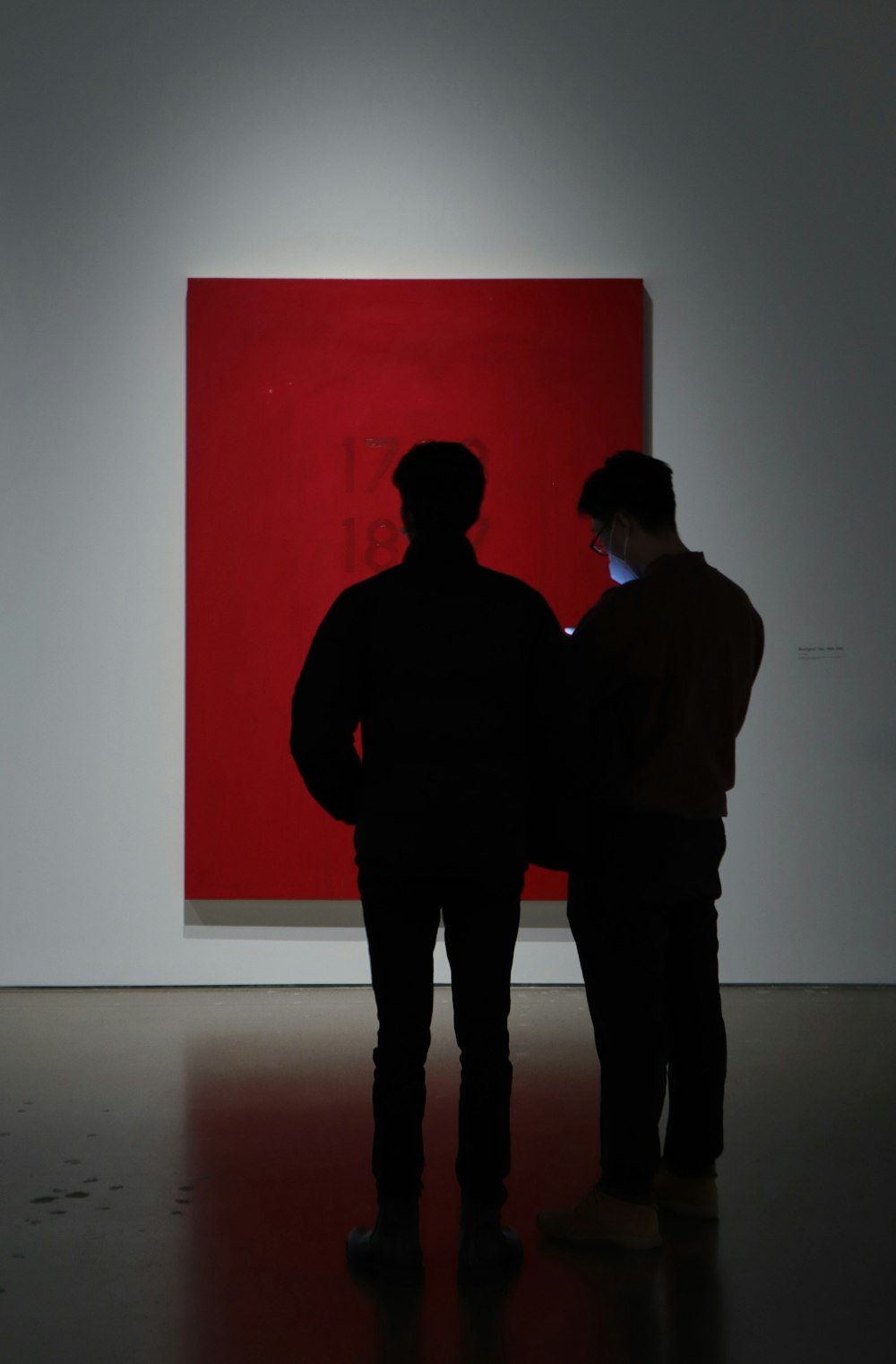 two people standing in front of a red painting