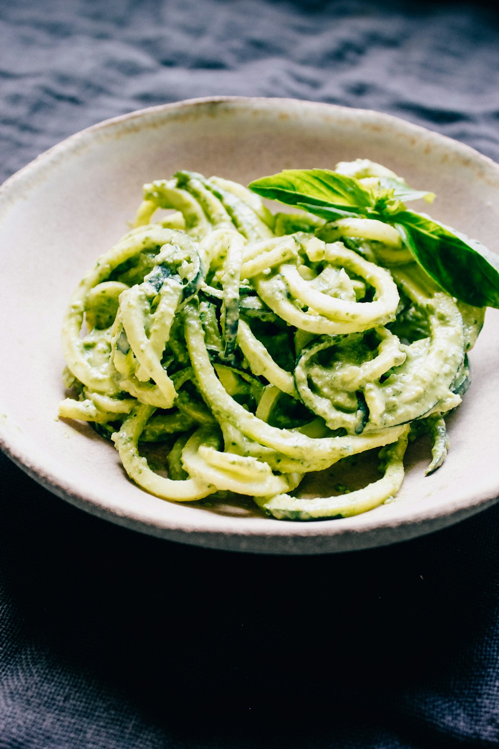 a white bowl filled with pesto pasta on top of a table