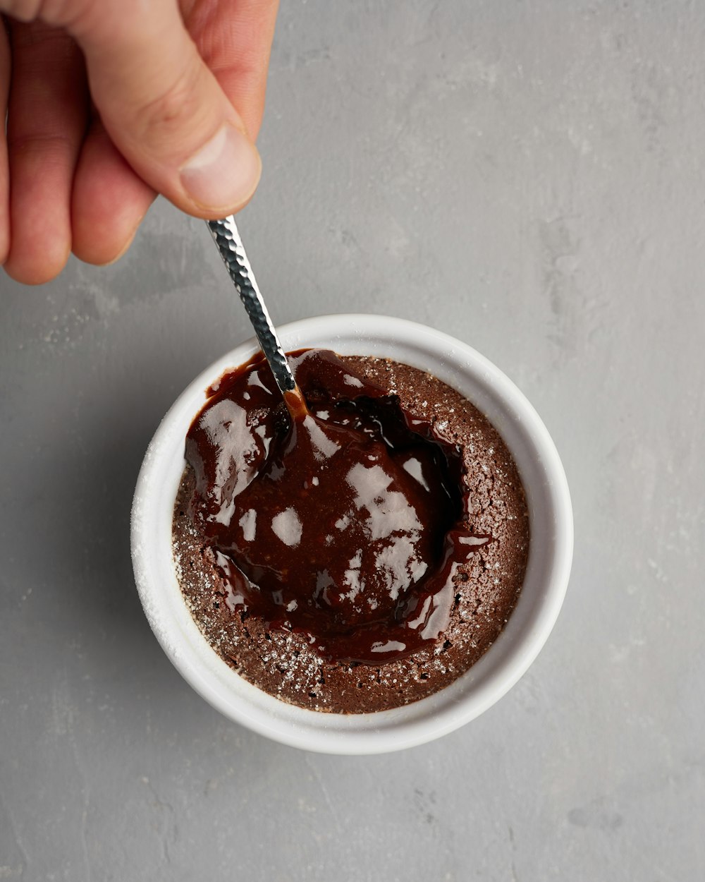 a hand holding a spoon over a bowl of chocolate cake