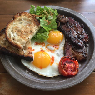 A hearty western-style breakfast plate featuring crispy bacon, eggs, toast, and grilled tomatoes on a cream ceramic dish.