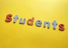 Colorful letters arranged to spell 'students' against a bright yellow background. Each letter is decorated with different patterns, such as polka dots, stripes, and checkered designs.