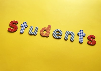 Colorful letters arranged to spell 'students' against a bright yellow background. Each letter is decorated with different patterns, such as polka dots, stripes, and checkered designs.