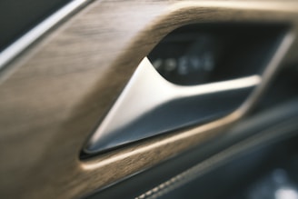 A close-up view of a car interior detail featuring a metallic door handle set in a wood-textured panel.