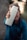 A person is holding a white water bottle prominently towards the camera, with a blurred background. The focus is on the bottle, which has a simple design with a clear lid.