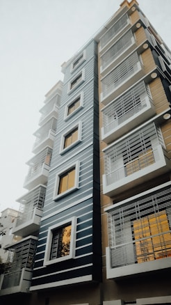 A modern multi-story residential building with a sleek design, featuring horizontal lines and large windows. The building is characterized by a mix of blue, white, and beige colors.