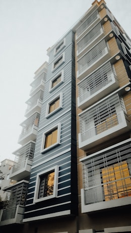 A modern multi-story residential building with a sleek design, featuring horizontal lines and large windows. The building is characterized by a mix of blue, white, and beige colors.