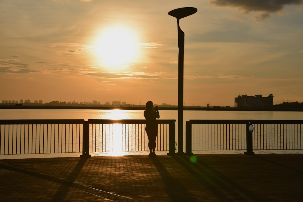 a person standing on a pier watching the sun set