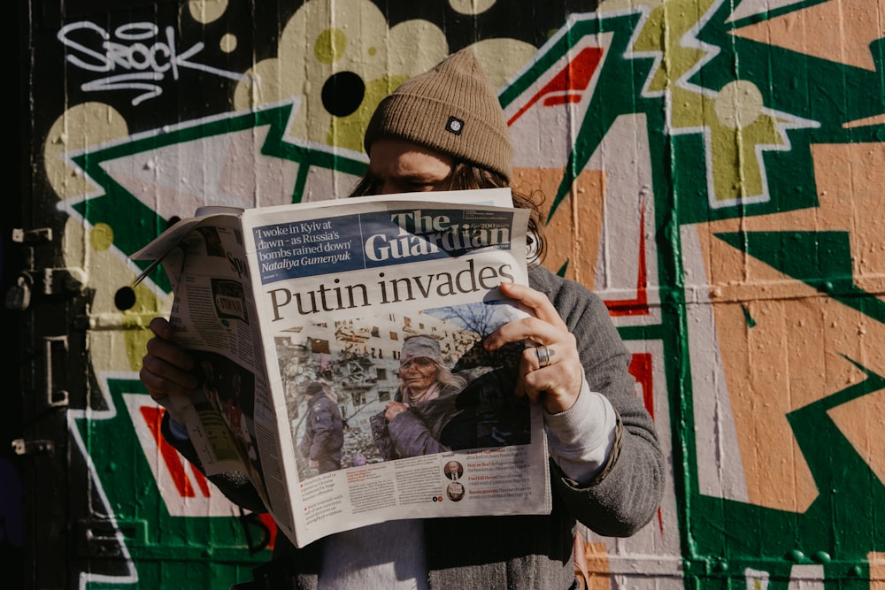 Ein Mann liest eine Zeitung vor einer mit Graffiti bedeckten Wand
