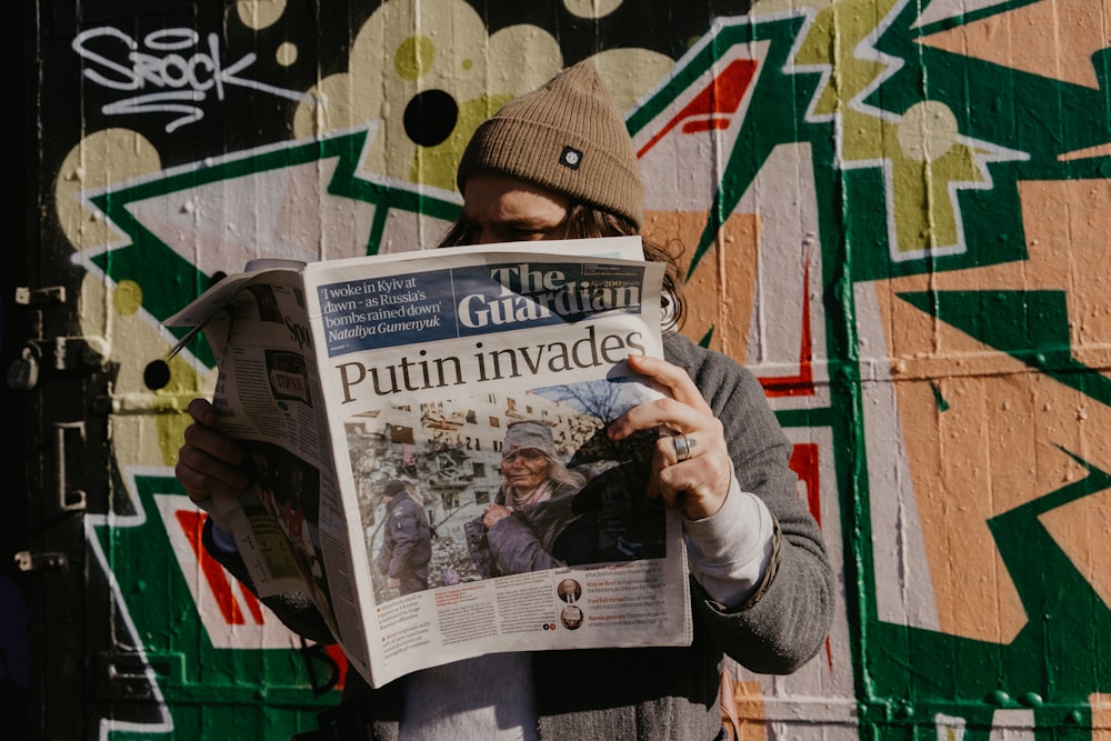 a man reading a newspaper in front of a graffiti covered wall