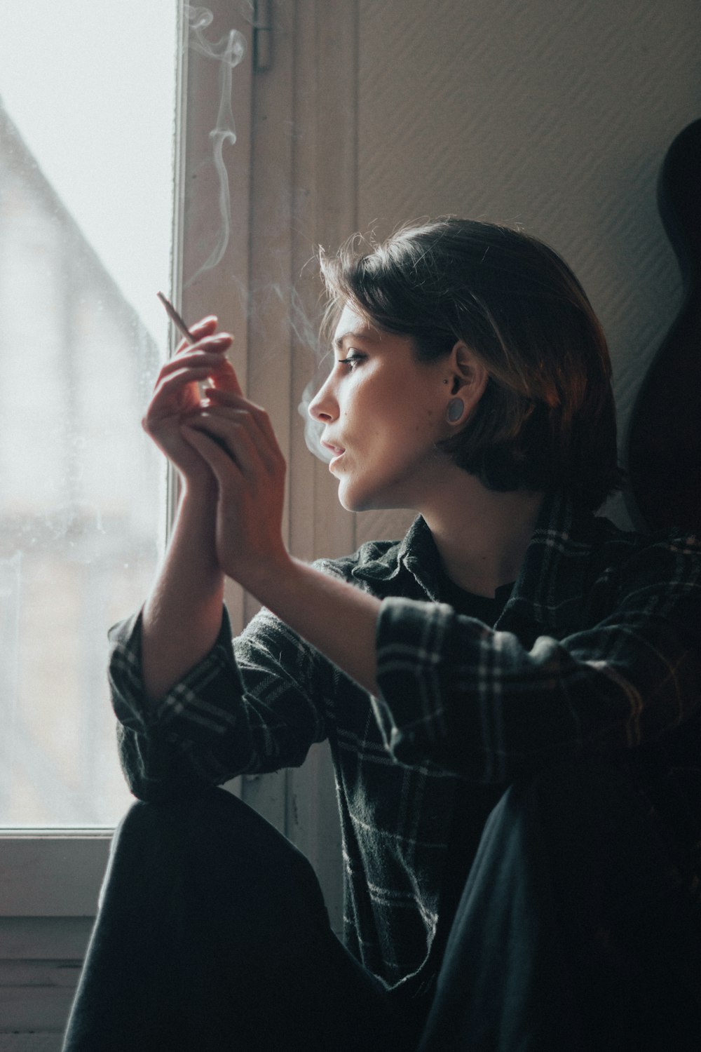 a woman sitting on a window sill smoking a cigarette