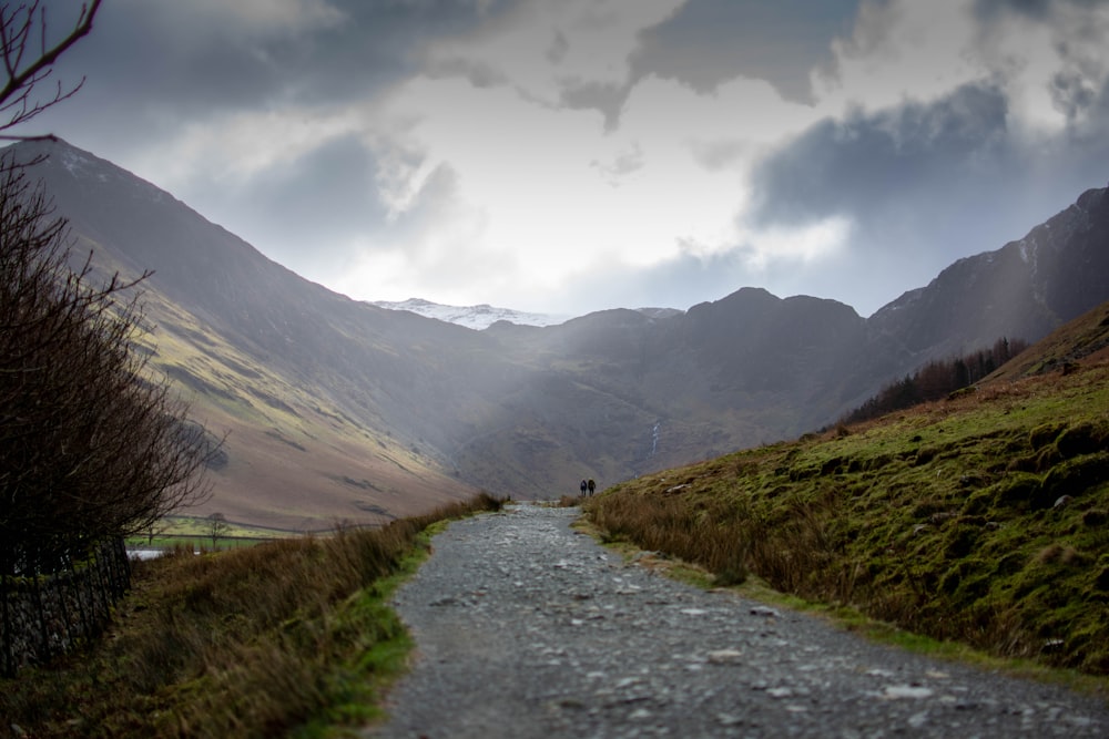 a dirt road surrounded by mountains under a cloudy sky