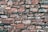 A wall made of irregularly shaped stones stacked closely together. The stones vary in size and have a rough, uneven texture with shades of brown and gray. Some stones have patches of lichen or moss, adding a natural element.