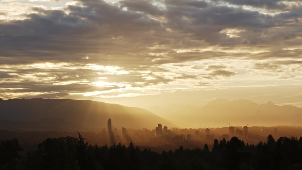 the sun is setting over a city with mountains in the background