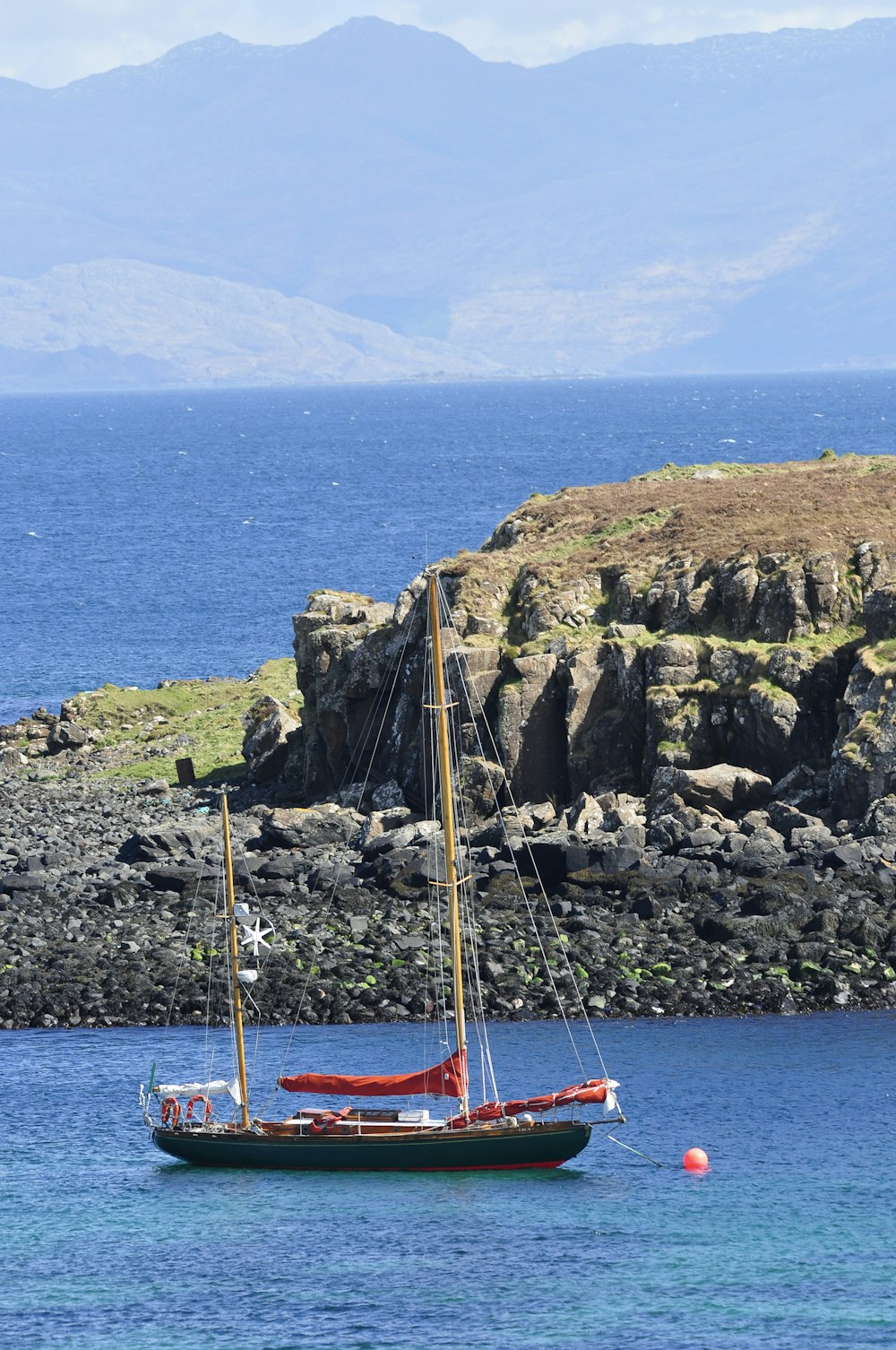 a sailboat in the water near a rocky shore