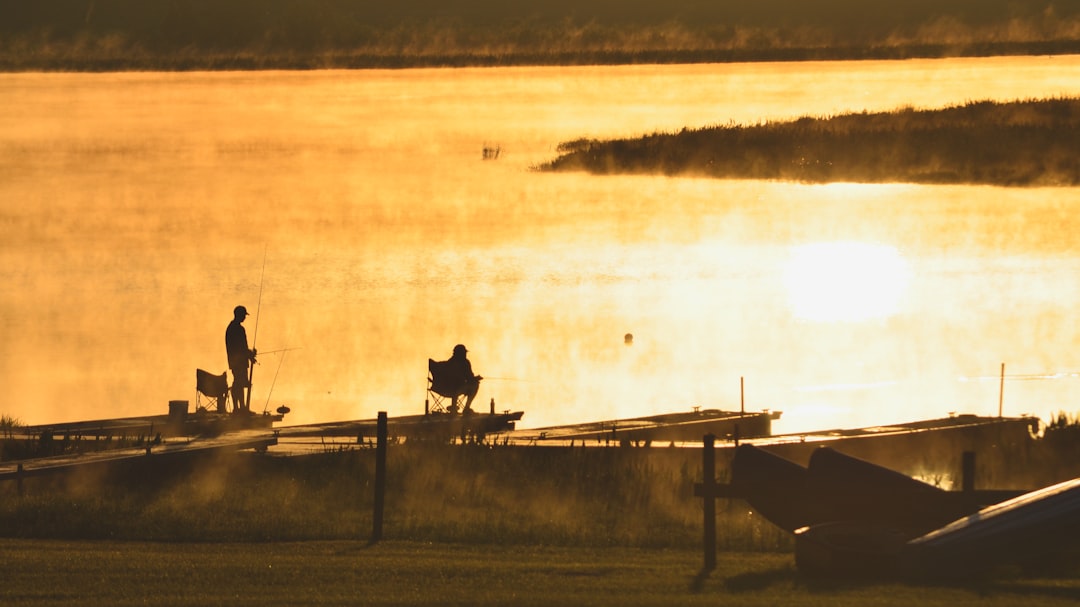 a couple of people standing on top of a boat, Early morning fishermen over a golden lake with the mist rising.