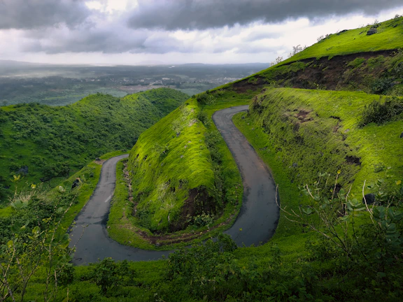 Wide-angle view of a winding road cutting through lush green hills under a dramatic sky.