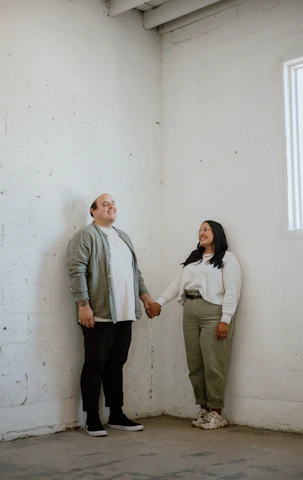A couple smiling and holding hands during a supportive coaching session in a bright, comfortable room.