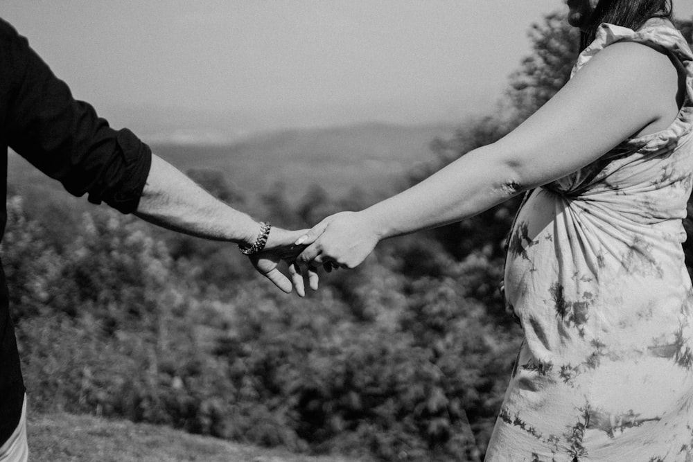 um homem e uma mulher de mãos dadas enquanto estão no topo de uma colina