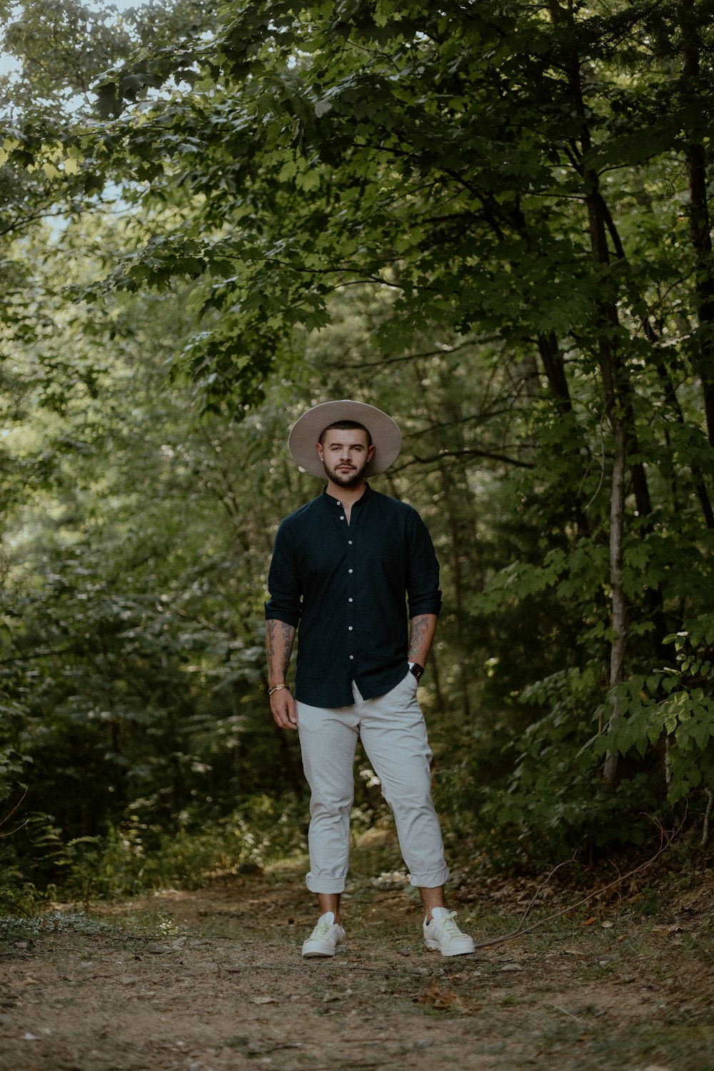 a man wearing a hat standing in the middle of a forest