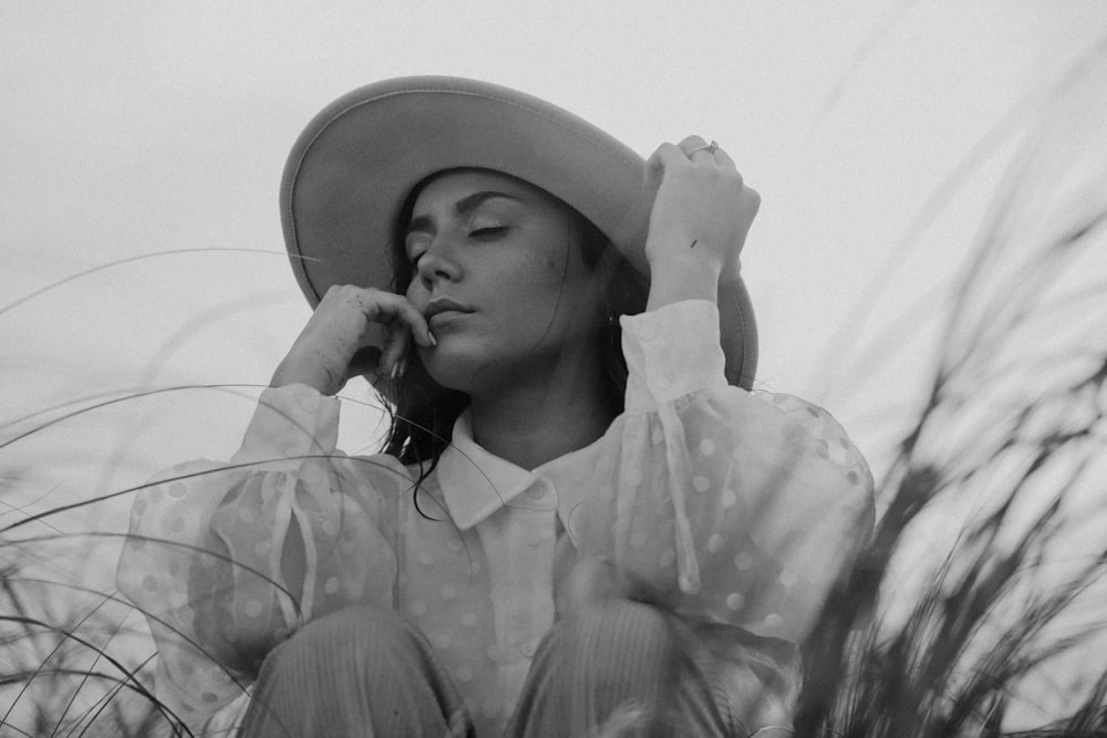 a woman wearing a hat sitting in tall grass