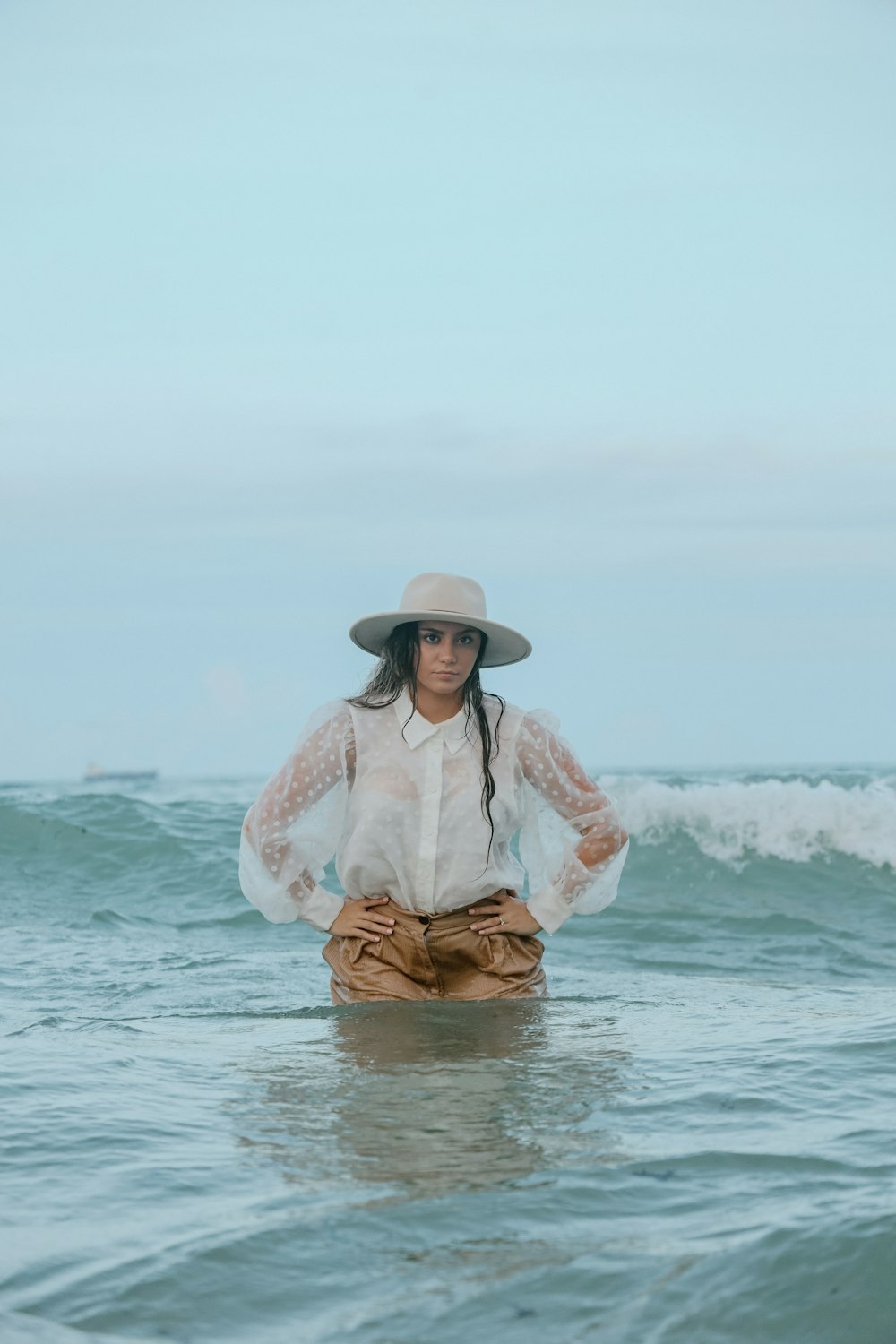 a woman standing in the ocean wearing a hat