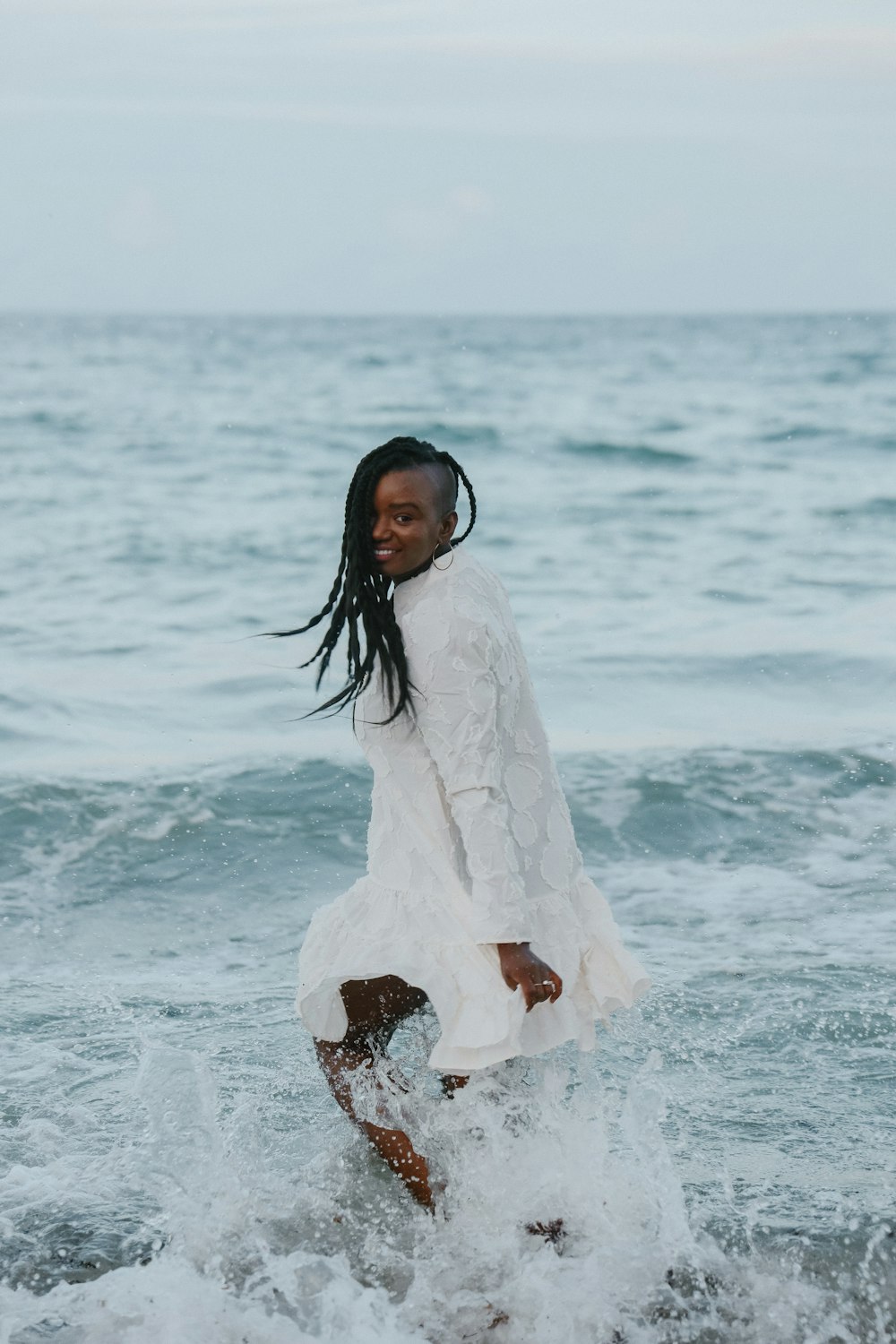 uma mulher em um vestido branco de pé no oceano