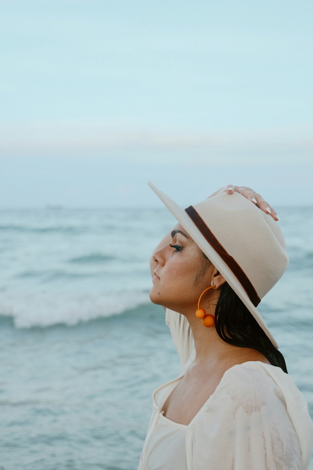 a woman wearing a hat standing in front of the ocean