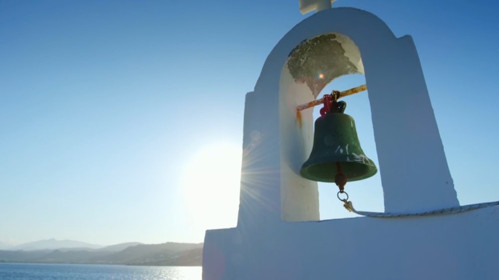 a bell on the side of a building near a body of water