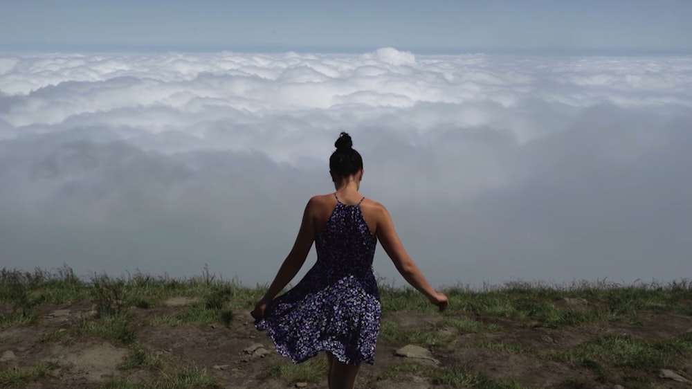 a woman standing on top of a hill above the clouds