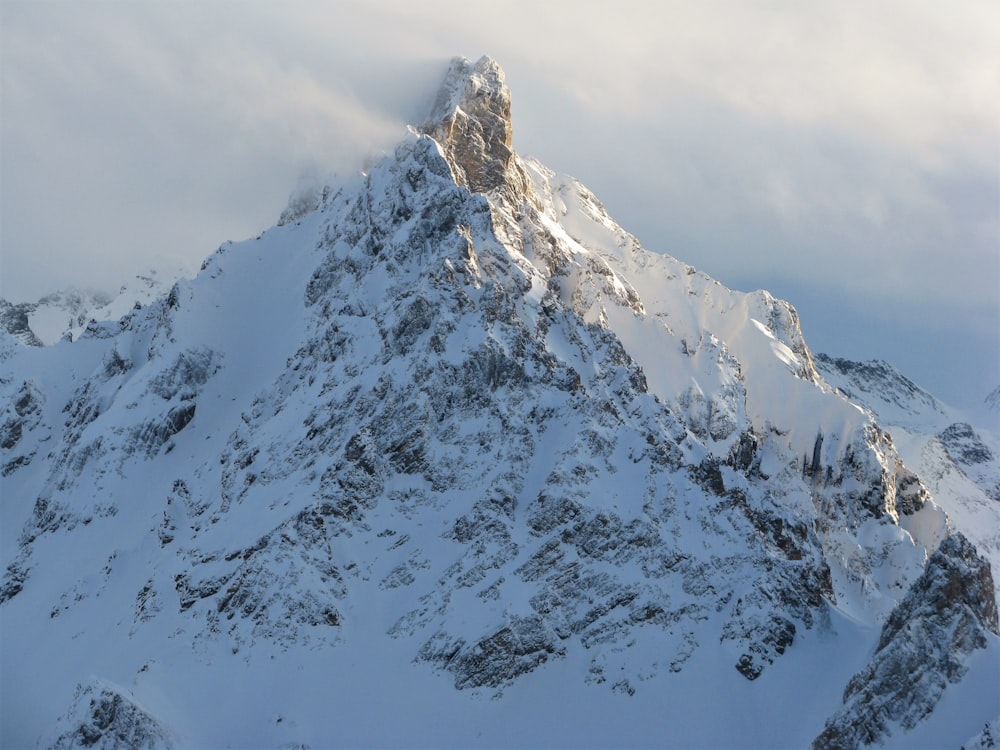 a very tall mountain covered in snow under a cloudy sky