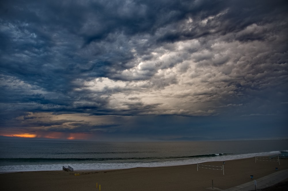 a cloudy sky over a beach with a soccer goal in the foreground