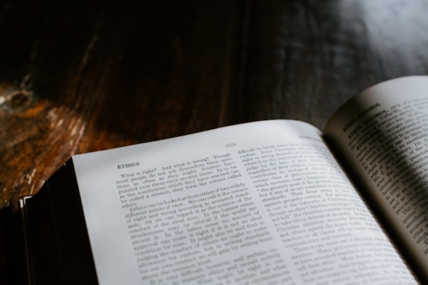 A book open to a page discussing ethics, with text printed in a serif font. The page is well-lit, making the text clearly visible, while the background and surrounding area are darker, creating a contrast between the page and the wooden surface beneath it.