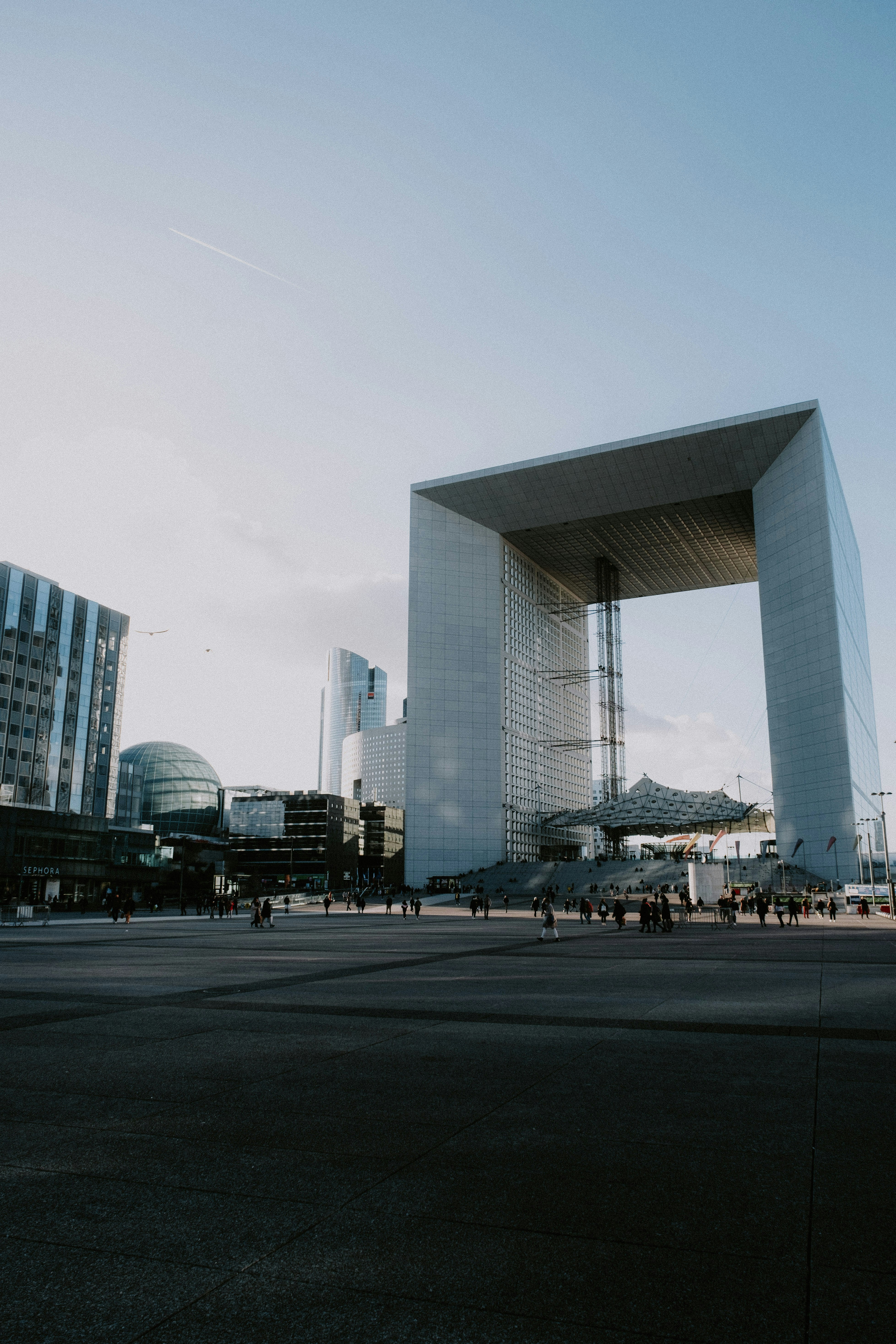 Modern city plaza with wide pedestrian walkways, urban infrastructure, public space with people walking, contemporary architecture