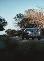 a black truck driving down a street next to trees