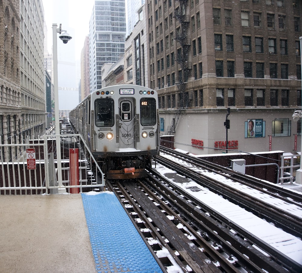 a silver train traveling down tracks next to tall buildings