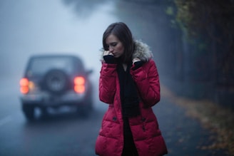 a woman standing in front of a car on a foggy road