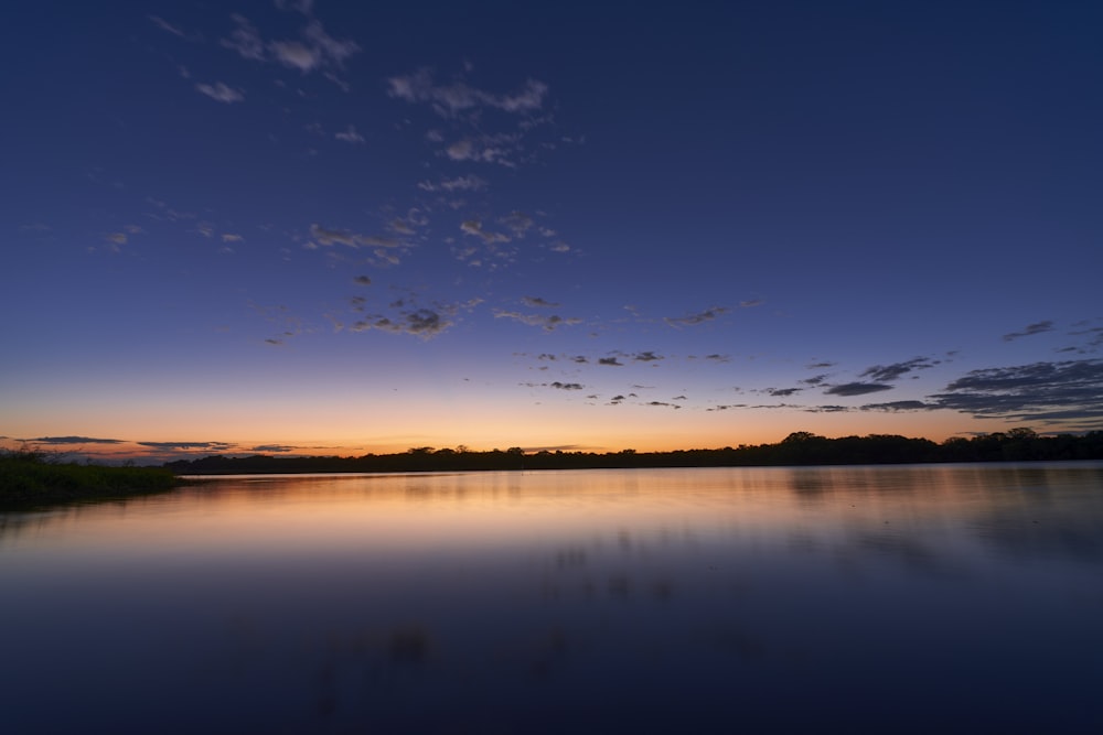 the sun is setting over a calm lake