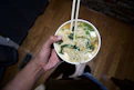 a person holding a bowl of noodles with chopsticks