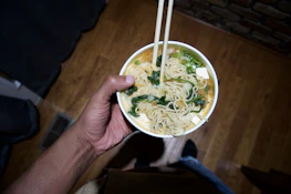 a person holding a bowl of noodles with chopsticks