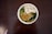 A white bowl is filled with a colorful array of ingredients including cubes of white tofu, finely chopped greens, and what appears to be fried shallots or onions.