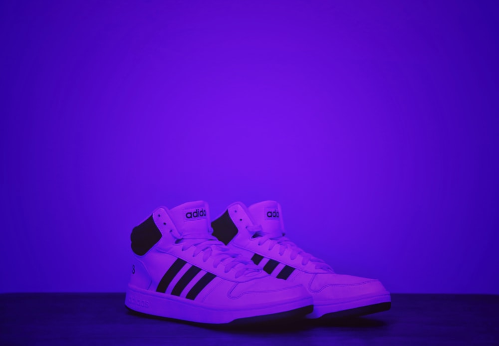 a pair of white and black sneakers against a purple background