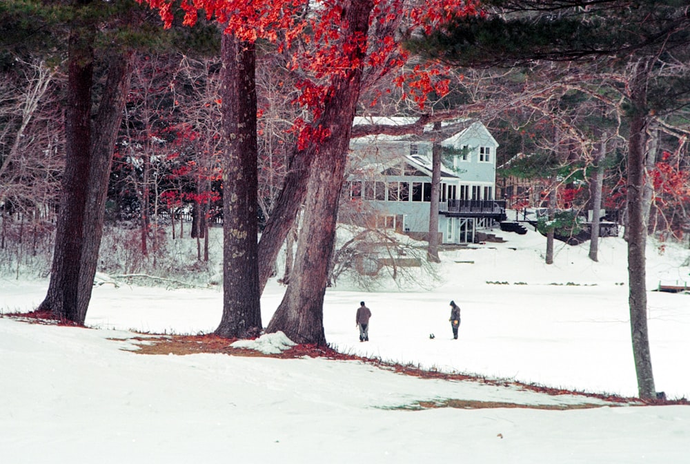 two people walking through the snow in front of a house